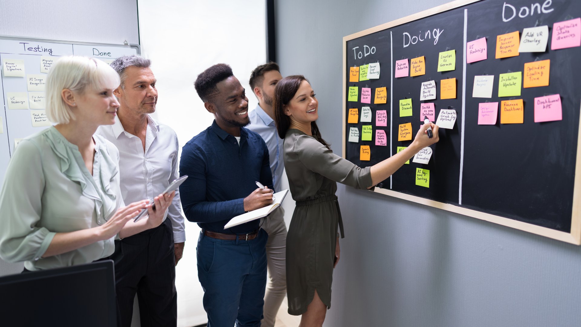A digital whiteboard with sticky notes, surrounded by a team collaborating during a workshop.